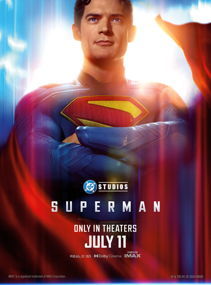 A promotional poster for the upcoming Superman movie by DC Studios. Superman, portrayed by a new actor, stands confidently with his arms crossed, illuminated by a bright white and blue light behind him. He wears the classic blue suit with a red and yellow "S" emblem on his chest and a flowing red cape. The text reads: "DC Studios SUPERMAN" on the left, and "ONLY IN THEATERS JULY 11" on the right, alongside logos for RealD 3D, Dolby Cinema, and IMAX.