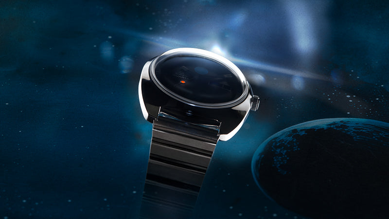 A futuristic angle view of the Q Timex 1975 Enigma Reissue watch, emphasizing the high-polish stainless steel case and integrated bracelet. The dial is barely visible in the shadows, but the orange seconds marker creates a striking contrast against the deep cosmic background with stars and planetary light flares.