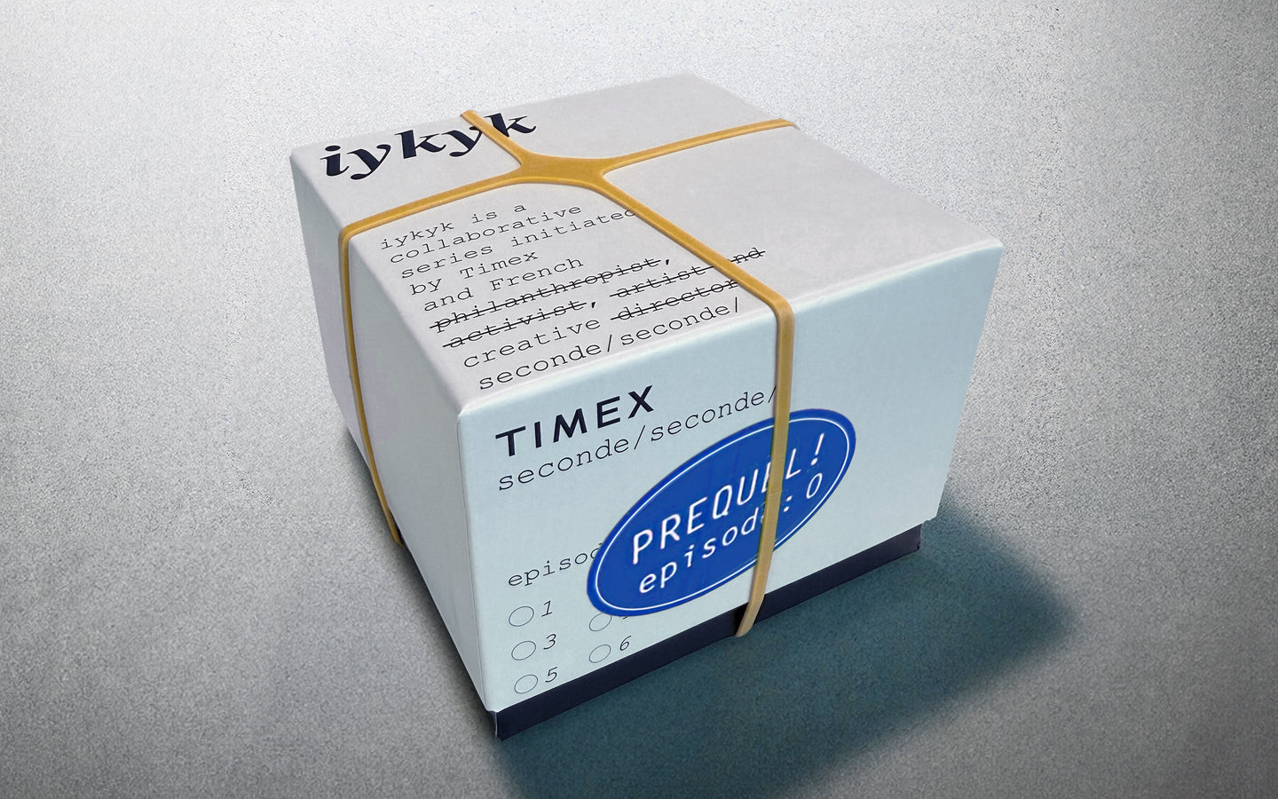 Timex x seconde/seconde/ Episode 0 packaging box, wrapped in yellow rubber bands. The box has black type with humorous strike-through edits and a blue sticker reading 'PREQUEL! episode: 0'.