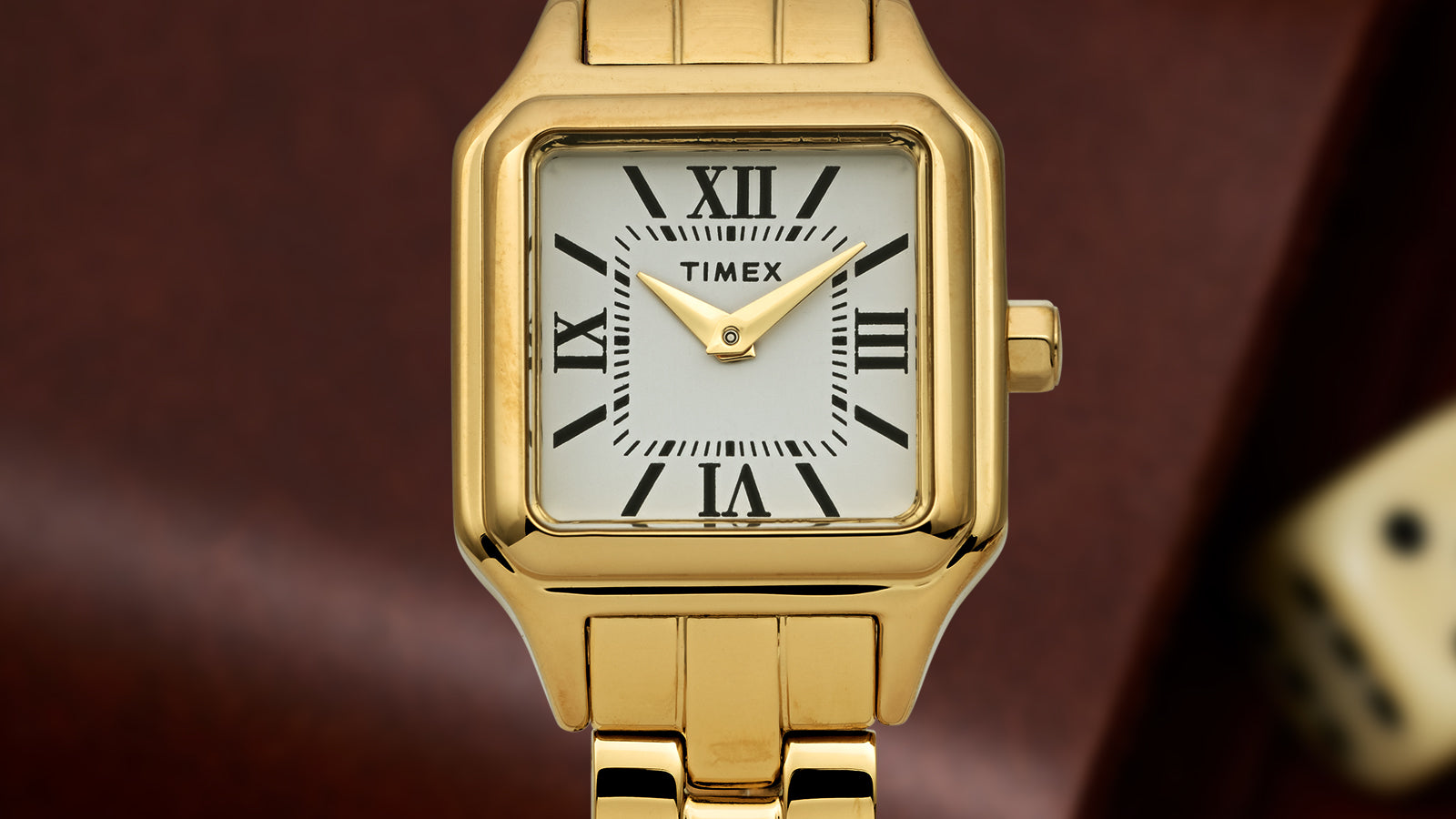 Close-up of the Timex Legacy Addison gold-tone watch showing square case, white dial with black Roman numerals, and gold hands on a link bracelet.