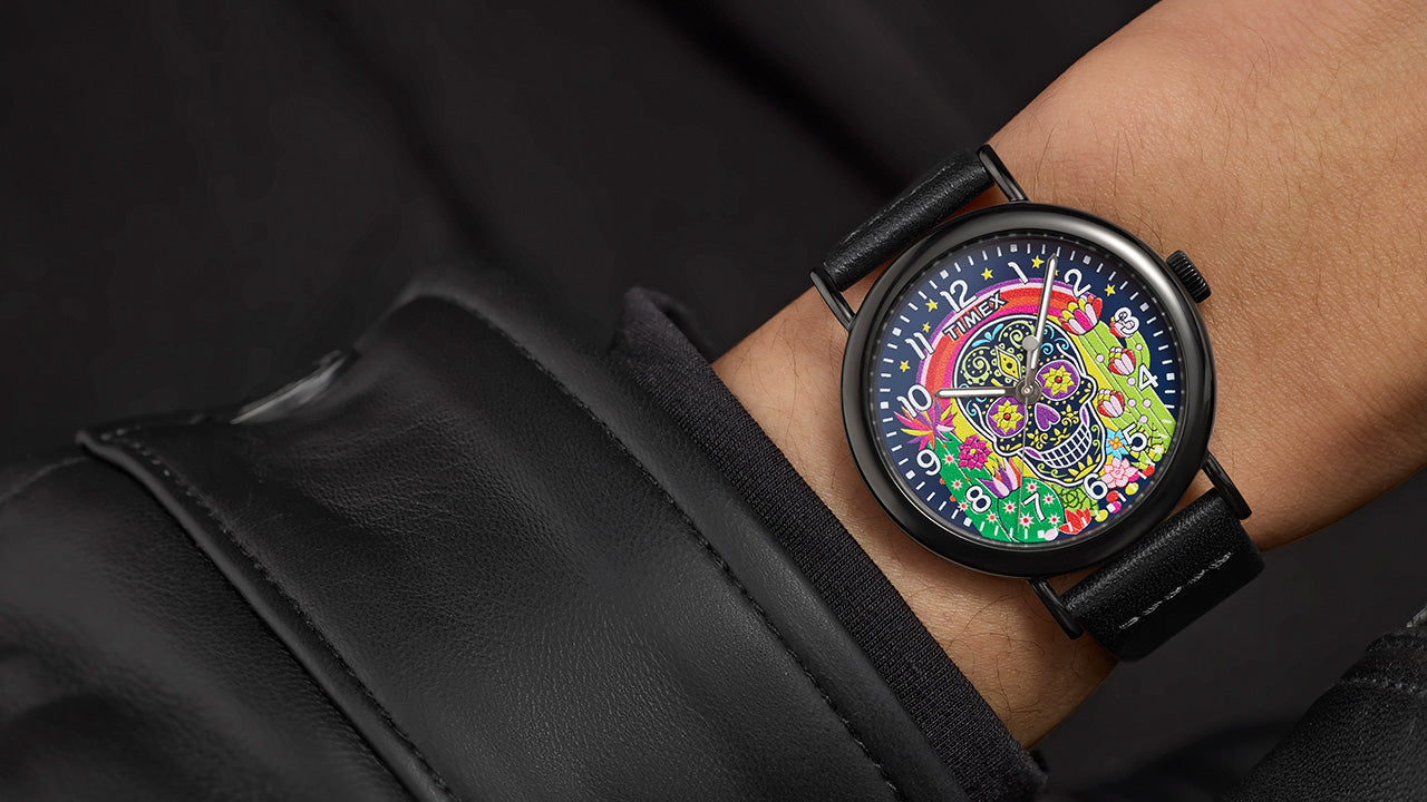 Timex Weekender Day of the Dead watch on wrist, with black leather strap and vibrant sugar skull dial design visible against a black jacket cuff.