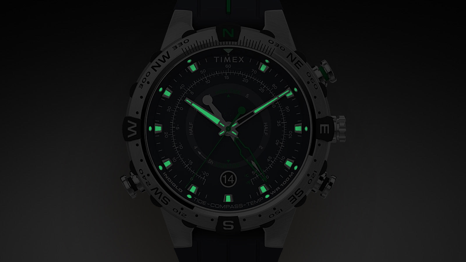 Timex Expedition Tide-Temp-Compass watch in dark setting with Indiglo backlight illuminating luminous hour markers and hands in bright green.