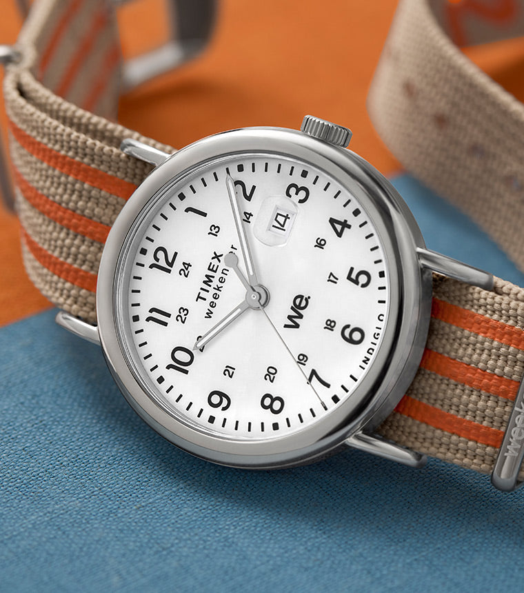 Timex Weekender laid on a textured surface with color blocks in orange and blue, featuring a beige and orange striped strap.