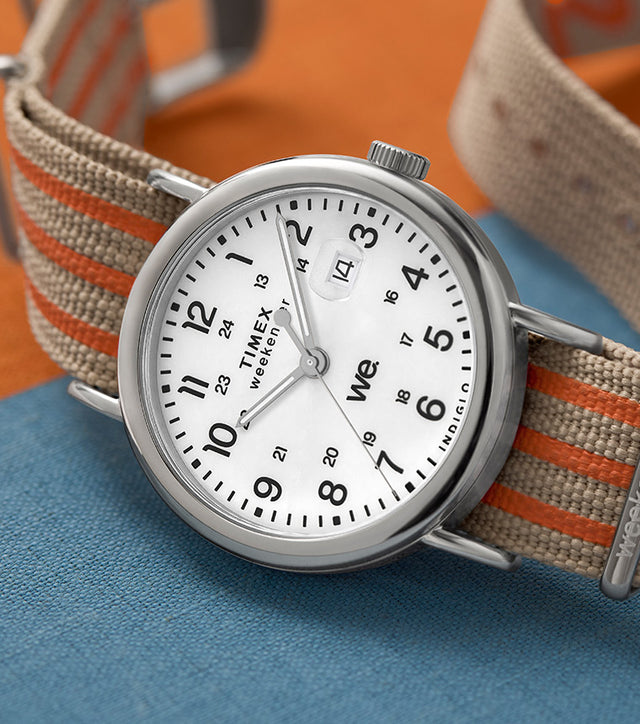 Timex Weekender laid on a textured surface with color blocks in orange and blue, featuring a beige and orange striped strap.