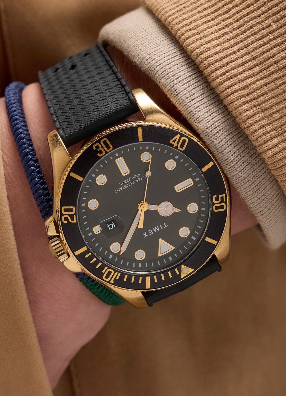 A Timex Harborside Coast watch with a green dial, gold-tone case, and black textured silicone strap rests on an antique-style world atlas cover. The black rotating bezel features gold markers, and the dial includes luminous hands and indices, with a magnified date window at 3 o’clock.