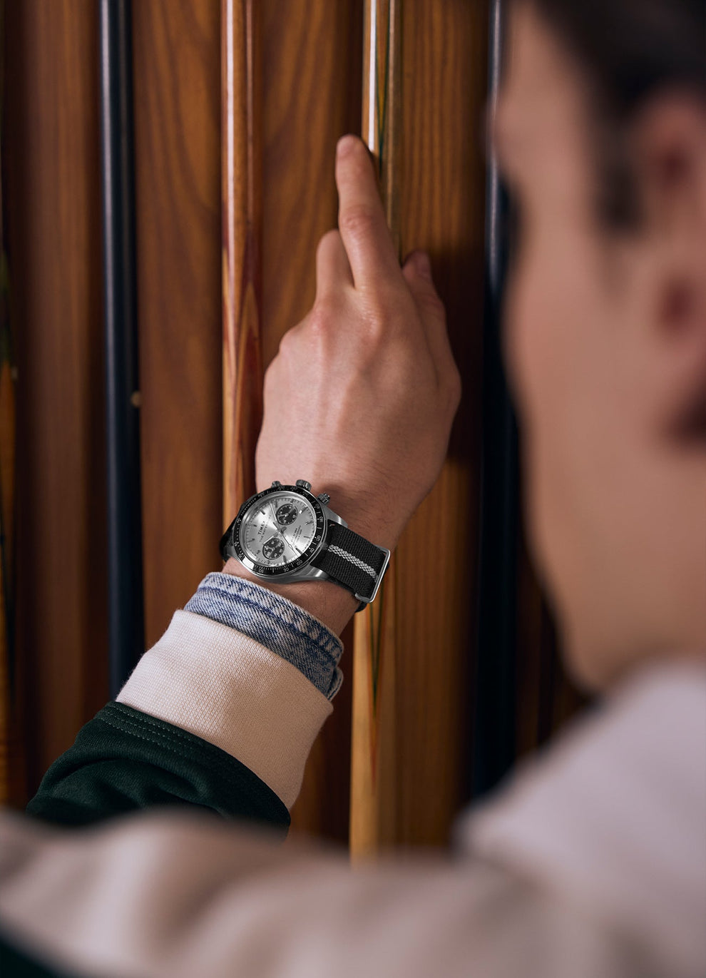 Lifestyle image of a male model wearing the Timex Waterbury Heritage Chronograph on his wrist while selecting a cue stick in a vintage-style wooden billiard rack, showing the watch’s clean, classic profile from a side angle.
