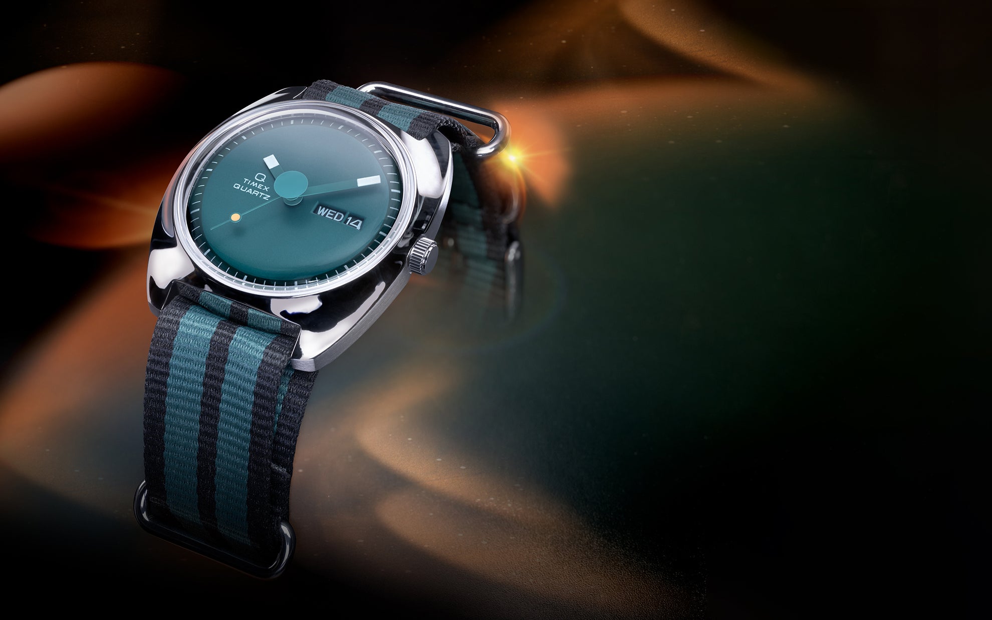 Stylized lifestyle image of the Q Timex® 1975 Enigma watch with a green dial and striped black-and-green NATO strap, illuminated by ambient orange and teal lighting against a cosmic-style background.
