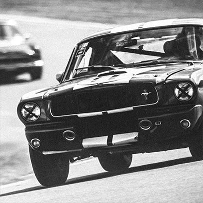 Monochrome image of a vintage racing car with the number 11 on the door, speeding along a blurred racetrack. The shot captures motion and energy, evoking the golden era of motorsports, aligning with the Q Timex racing chronograph theme.