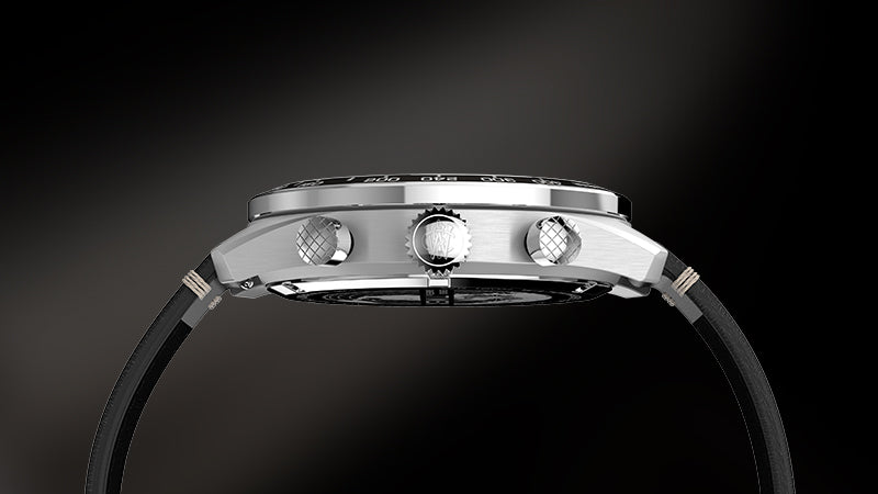 Side profile of the Timex Waterbury Chronograph, emphasizing the brushed stainless steel case, textured pushers, and signed crown with "W" engraving. The black leather strap attaches seamlessly to the slim case, all set against a dark gradient backdrop.