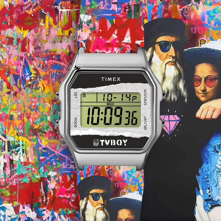 A bold digital Timex watch from the Timex x TVBoy collaboration is centered against a vibrant, graffiti-style background. The watch features a stainless steel case and digital display with custom artwork on the lower half of the face, including the TVBoy logo and a torn paper effect. Behind the watch is a colorful mural featuring pop art-style versions of Leonardo da Vinci and the Mona Lisa wearing modern sunglasses, set against an explosion of spray-painted textures and street art elements.