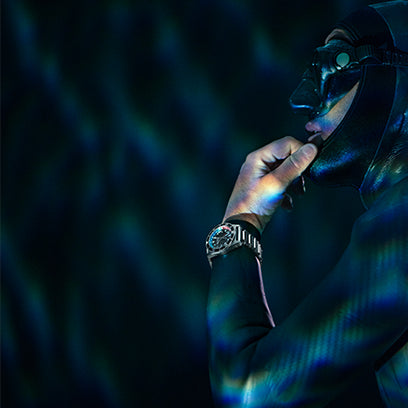 Side profile of a freediver adjusting mask strap underwater, light reflections playing across the Timex Deepwater Meridian 200 on their wrist.