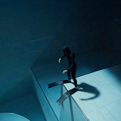 Freediver stands on an underwater ledge with fins on, preparing to dive deeper in a large pool.