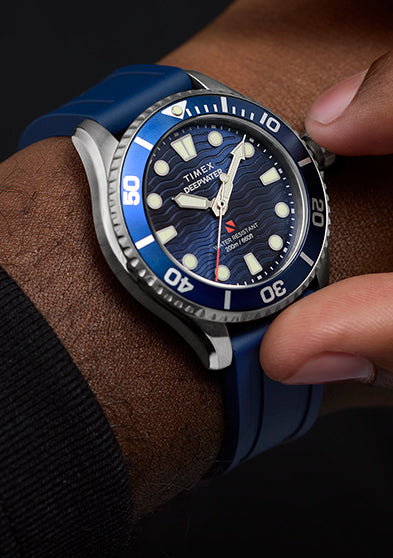 Close-up of a person wearing the Timex Deepwater Meridian 200 dive watch with a blue strap, adjusting the bezel.