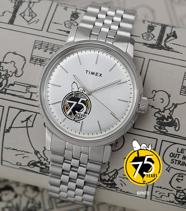 Timex x Peanuts® Marlin® Automatic watch placed over black-and-white Peanuts® comic strips, showing its silver-tone dial, minimalist indices, Snoopy illustration above the 75 Years logo, and open-heart movement view.