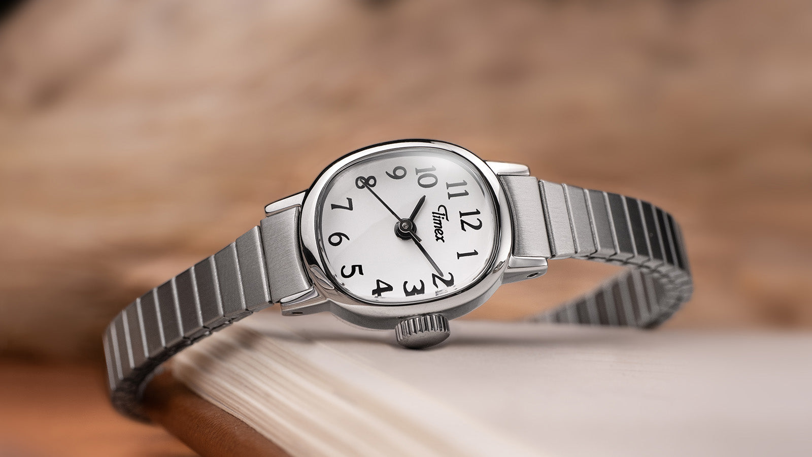 Timex Cavatina Mini watch with a silver expansion bracelet and white dial resting elegantly on the edge of an open book.