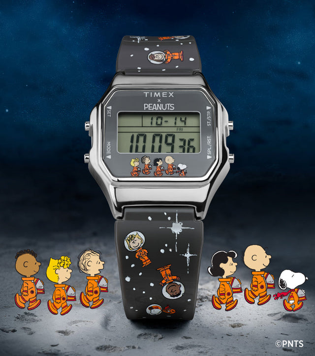 A Timex x Peanuts® T80 digital watch displayed on a lunar surface background with a starry night sky. The stainless steel square case frames a green digital display that shows the time, date, and alarm icons. Along the bottom of the display, Charlie Brown, Snoopy, Lucy, Linus, Franklin, and Woodstock appear in orange space suits. The black resin strap is decorated with white stars and Peanuts space-themed illustrations.