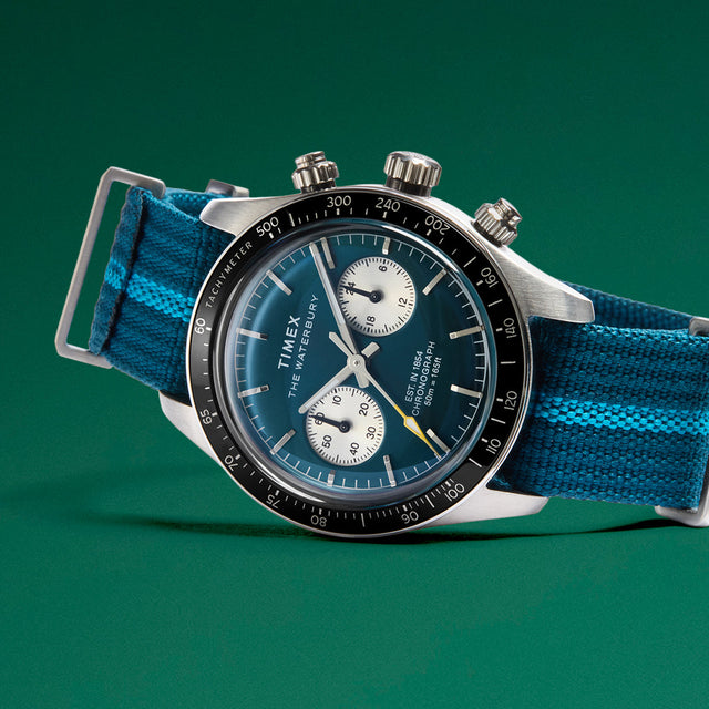 Close-up of Timex Waterbury Heritage Chronograph featuring a polished stainless-steel case, blue dial, and chronograph subdials with yellow detailing.