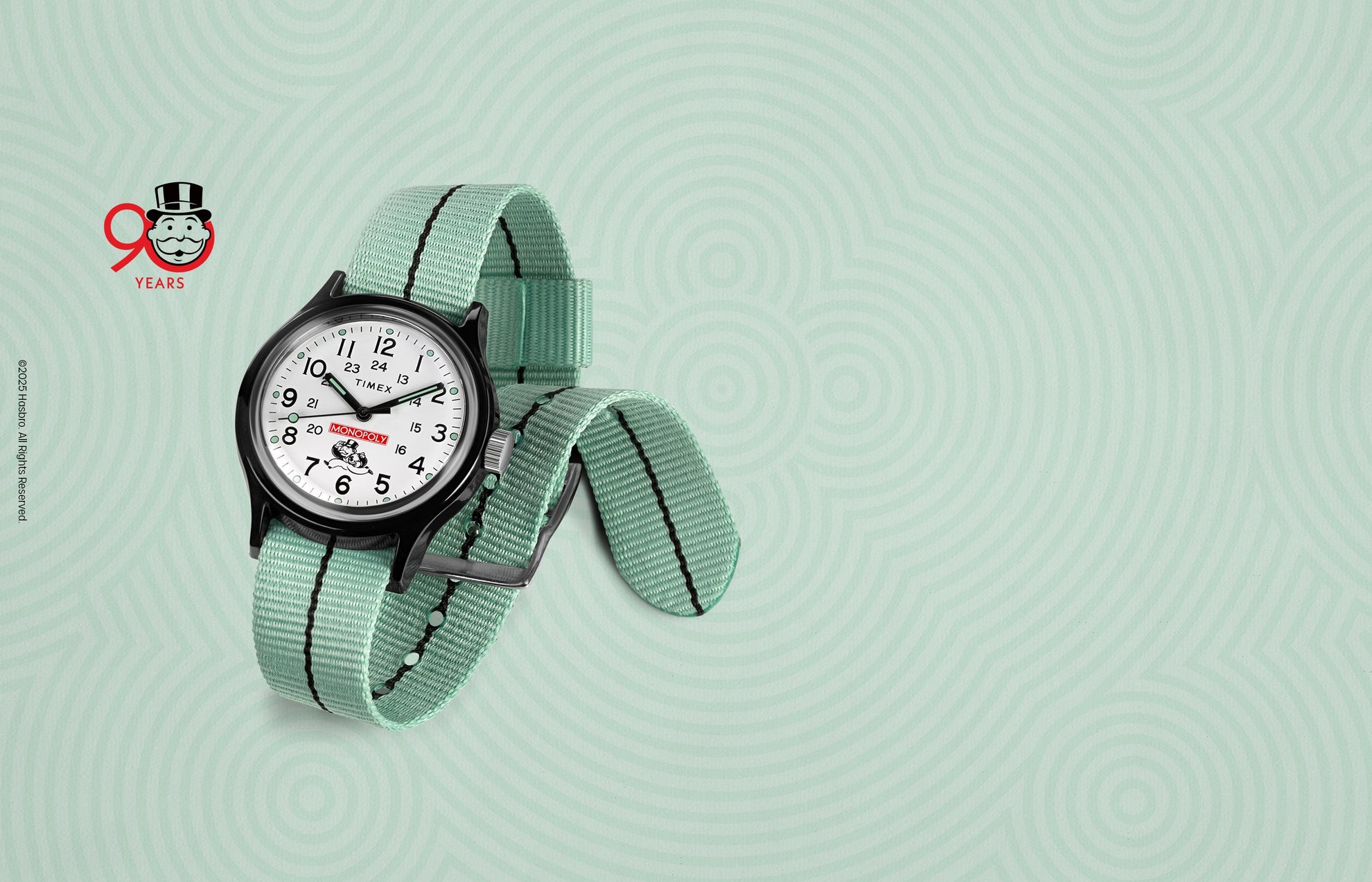 A Timex x Monopoly MK1 wristwatch featuring a crisp white dial with black numerals, a red Monopoly logo above the 6 o’clock position, and the Monopoly mascot holding a money bag. The watch has a black case and a mint-green nylon strap. A “90 Years” Monopoly anniversary logo appears in the background.
