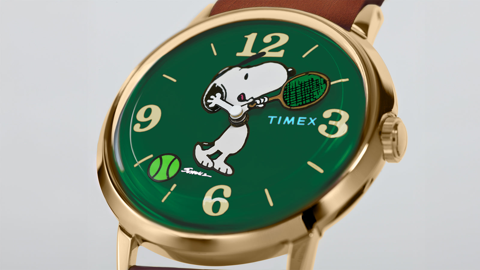 Angled close-up of the Peanuts® x Timex Marlin® Hand-Wound watch featuring Snoopy swinging a tennis racket on the green dial, with a tennis ball near 7 o’clock.