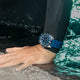 Diver’s arm partially submerged, wearing the Timex Deepwater Reef 200 with blue strap and bezel, illuminated by glistening surface water under bright light.