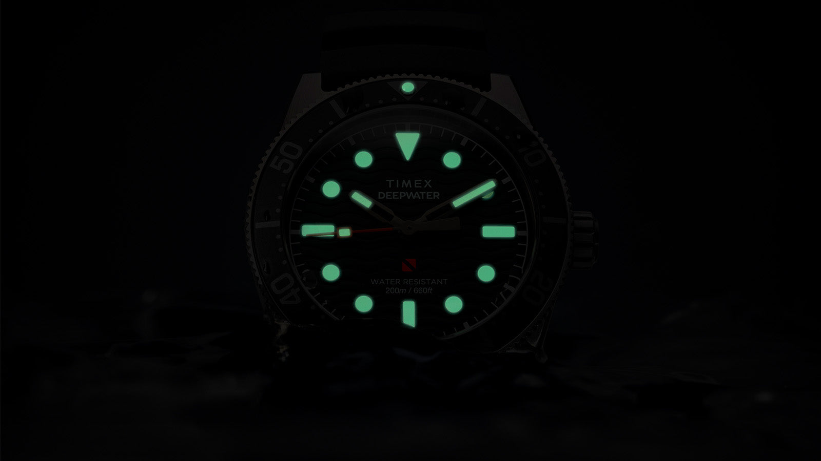 Timex Deepwater Reef 200 watch glowing in darkness, with bright green lume on the hands and hour markers, emphasizing superior underwater visibility.