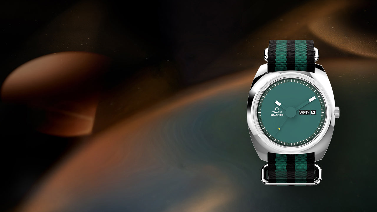 Full product image of the Q Timex® 1975 Enigma watch with teal dial and striped nylon strap centered against an abstract dark cosmic background, highlighting its 1970s-inspired design.