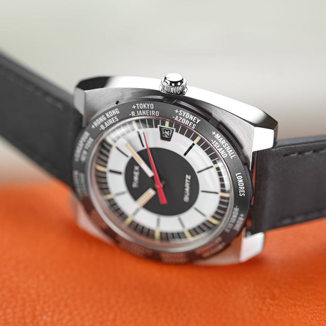 Close-up angled view of the Timex World Time Reissue watch showing the crown, raised acrylic crystal, and engraved world time bezel with city names such as Tokyo, Sydney, and London.
