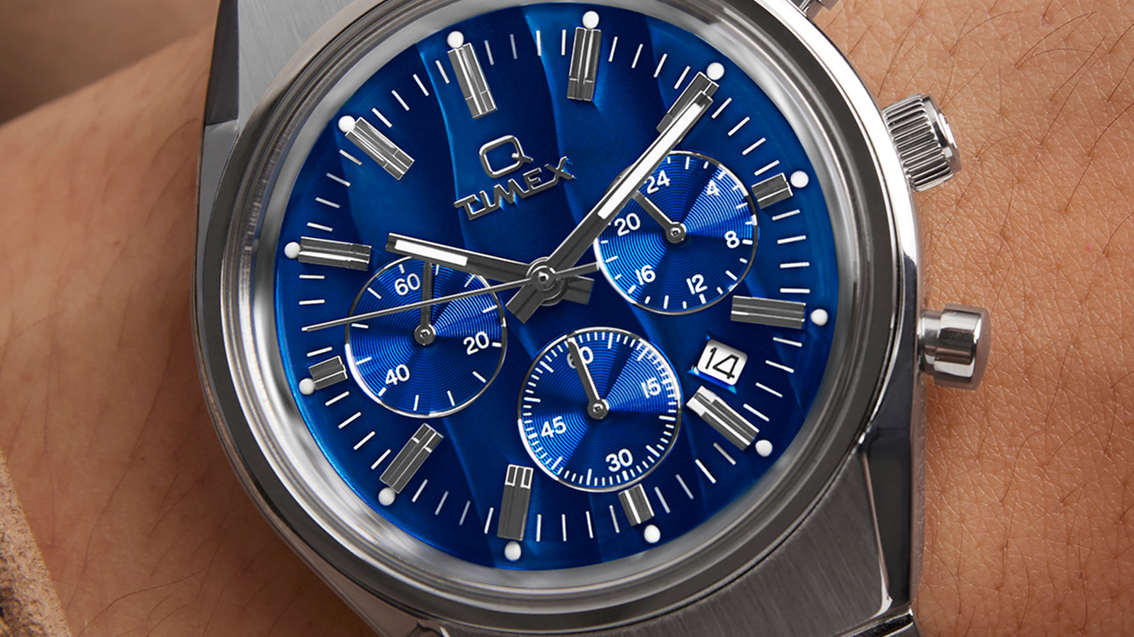 Wrist shot of the Q Timex Falcon Eye Chronograph with vibrant metallic blue dial, polished pushers, and integrated stainless-steel bracelet worn with a tan suede jacket.