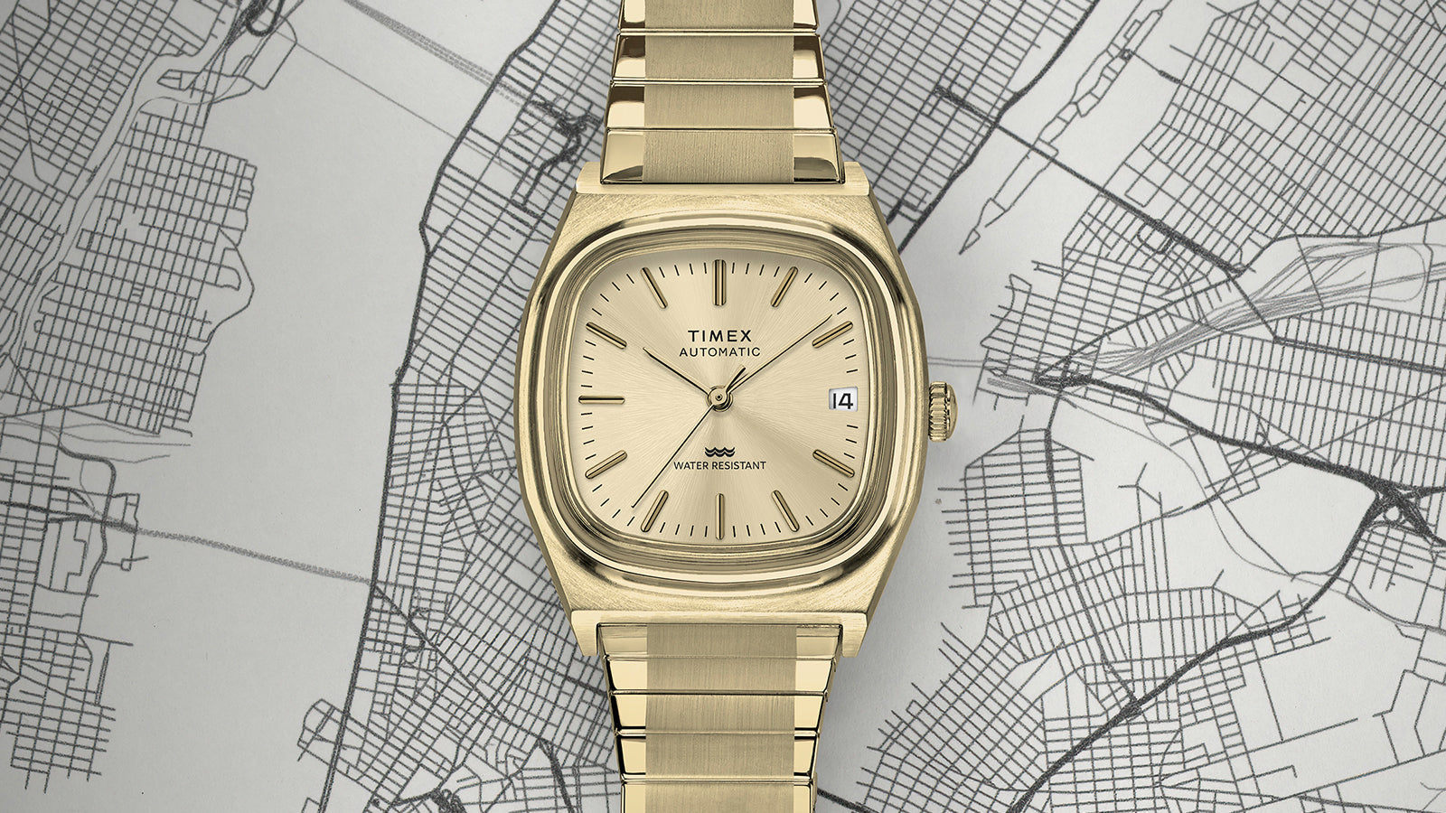 Top-down view of the gold-tone Timex® Automatic 1983 E Line Reissue highlighting its square cushion case, champagne dial, and integrated bracelet laid flat on a map background.