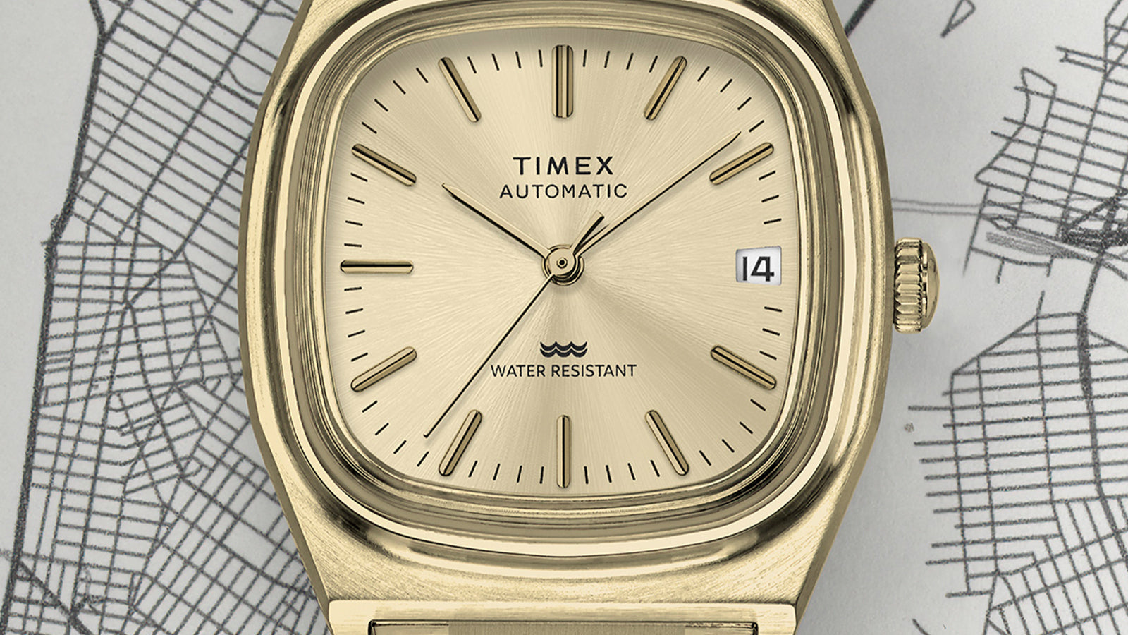 Macro shot of the Timex® Automatic 1983 E Line Reissue dial featuring gold-tone hands and hour markers, a date window at 3 o’clock, and minimalist branding.