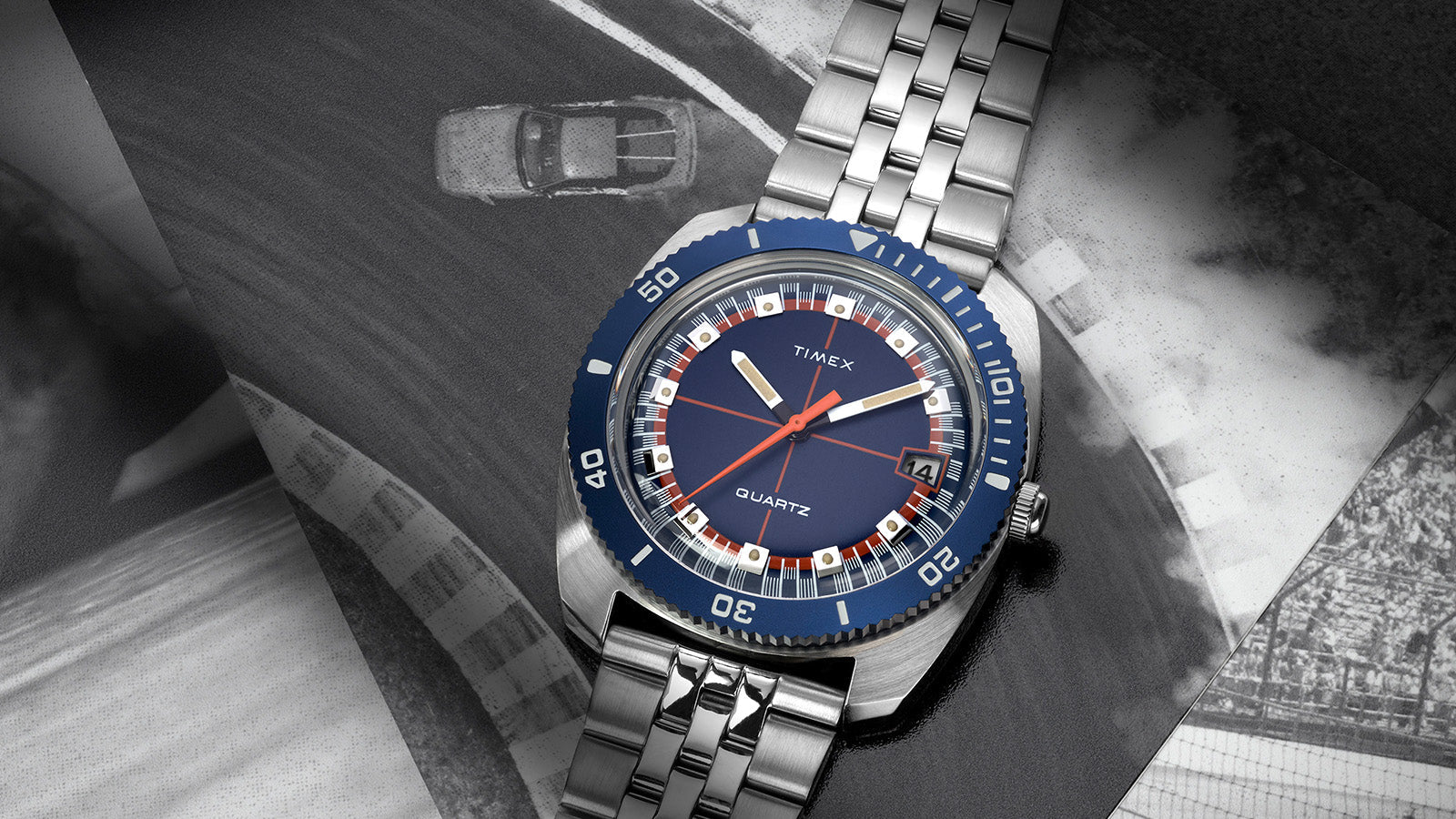 Q Timex® 1971 Velocity watch resting on black-and-white racing imagery, showcasing the bold orange seconds hand and geometric hour markers.