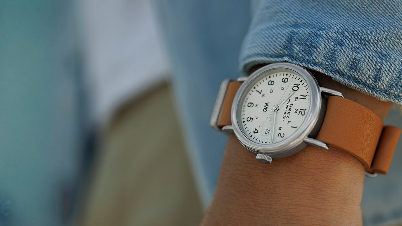Timex Weekender with white dial and tan leather strap worn on the wrist, styled with a light denim shirt.