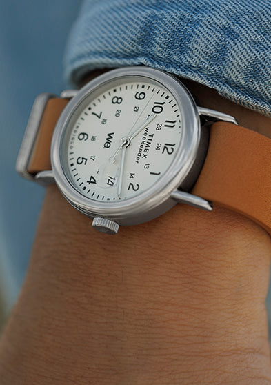 Timex Weekender with white dial and tan leather strap worn on the wrist, styled with a light denim shirt.