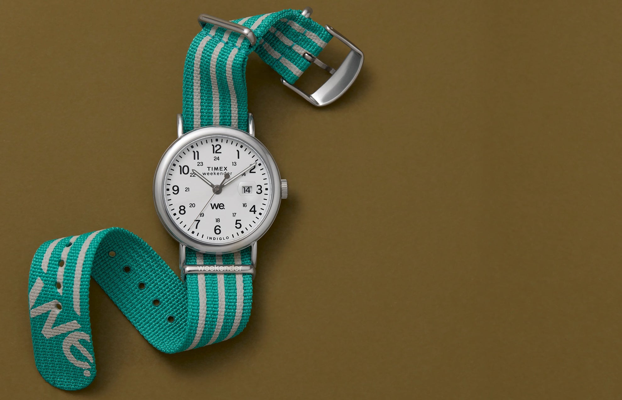 A Timex Weekender watch with a white dial, black numerals, and a teal-and-white striped fabric strap, displayed against a brown background.