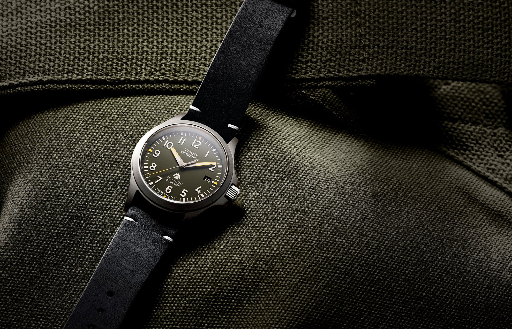 The Timex Expedition Titanium displayed flat on olive-green textured fabric, showcasing its brushed titanium case and classic field watch design.