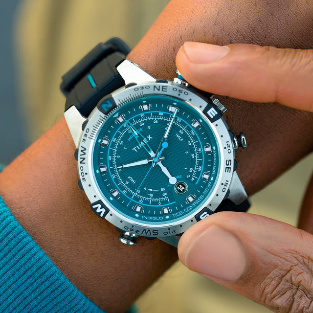 A person adjusting the crown of the Timex Expedition Tide-Temp-Compass on their wrist, showing the detailed teal dial, compass bezel, and textured black strap.