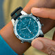 A person adjusting the crown of the Timex Expedition Tide-Temp-Compass on their wrist, showing the detailed teal dial, compass bezel, and textured black strap.