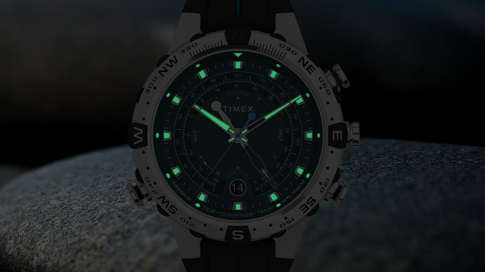 The Timex Expedition Tide-Temp-Compass glowing in low light with green luminescent indices and hands, enhancing nighttime readability.