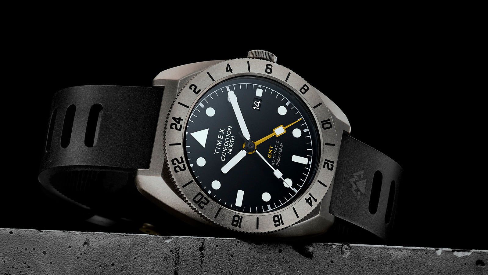 Angled view of the Timex Expedition North GMT Titanium Automatic on a textured black surface, emphasizing the 24-hour bezel and robust case design.