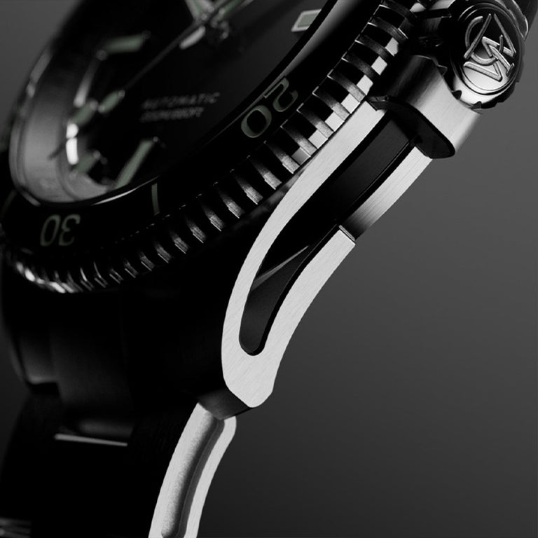 Macro side view of Timex Atelier watch case with brushed stainless steel finish, detailed crown engraved with "T" logo, and knurled bezel edge.