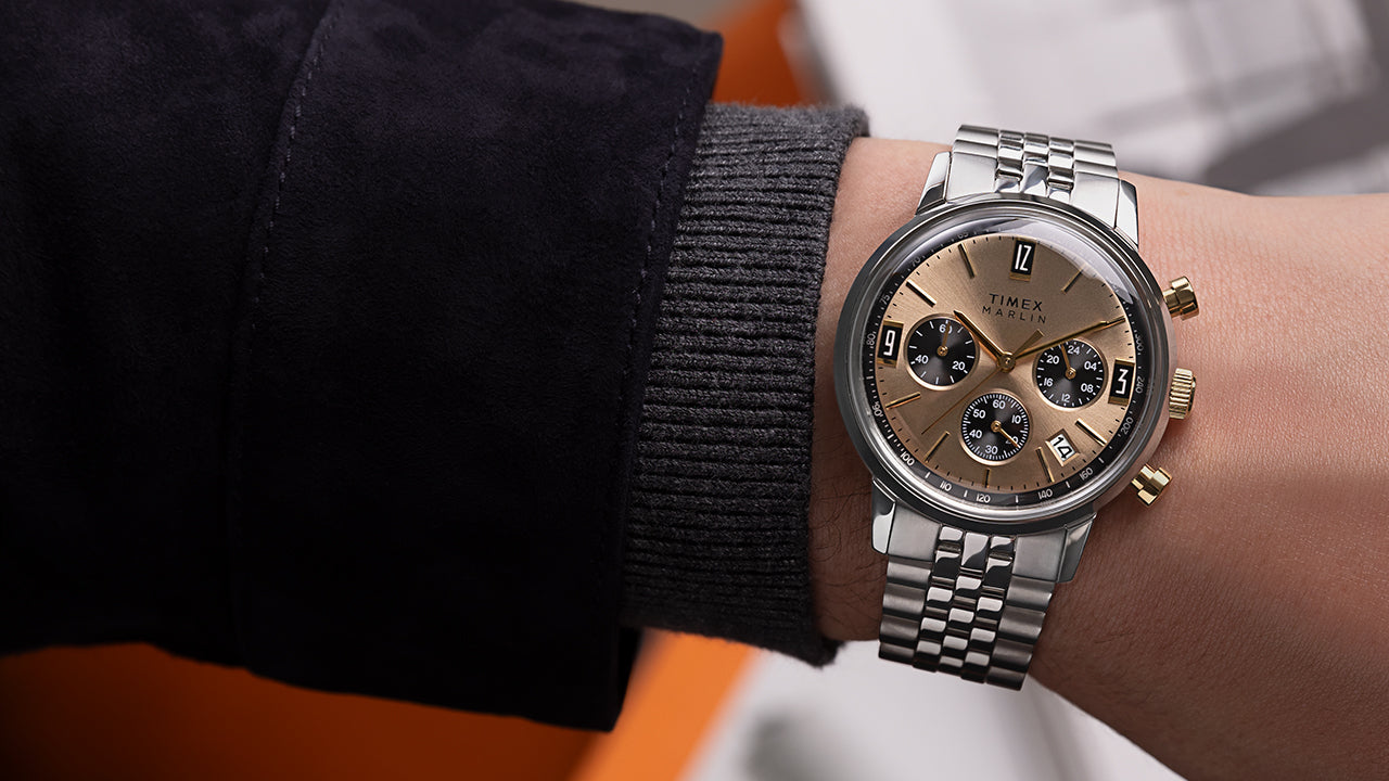 Close-up wrist shot of Timex Marlin Chronograph Tachymeter with champagne dial and stainless-steel bracelet, styled with gray knit cuff.