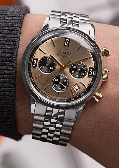 Close-up wrist shot of Timex Marlin Chronograph Tachymeter with champagne dial and stainless-steel bracelet, styled with gray knit cuff.