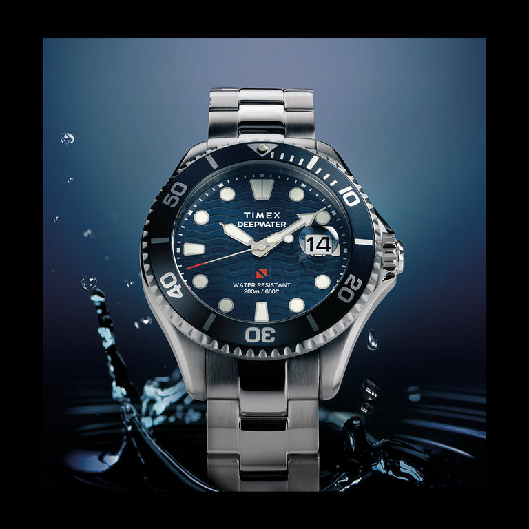 Timex Deepwater automatic dive watch with a blue wave-textured dial, luminous markers, and stainless steel bracelet surrounded by water splashes.