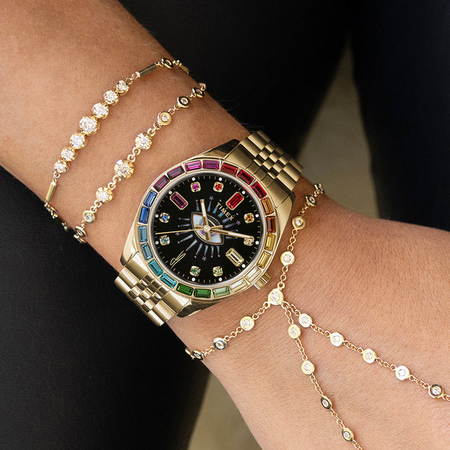 Close-up of the Timex x Jacquie Aiche “Cosmic Nights” watch face showing the radiant eye design at the center, gold hands, and a bezel set with rainbow-hued stones symbolizing energy and light.