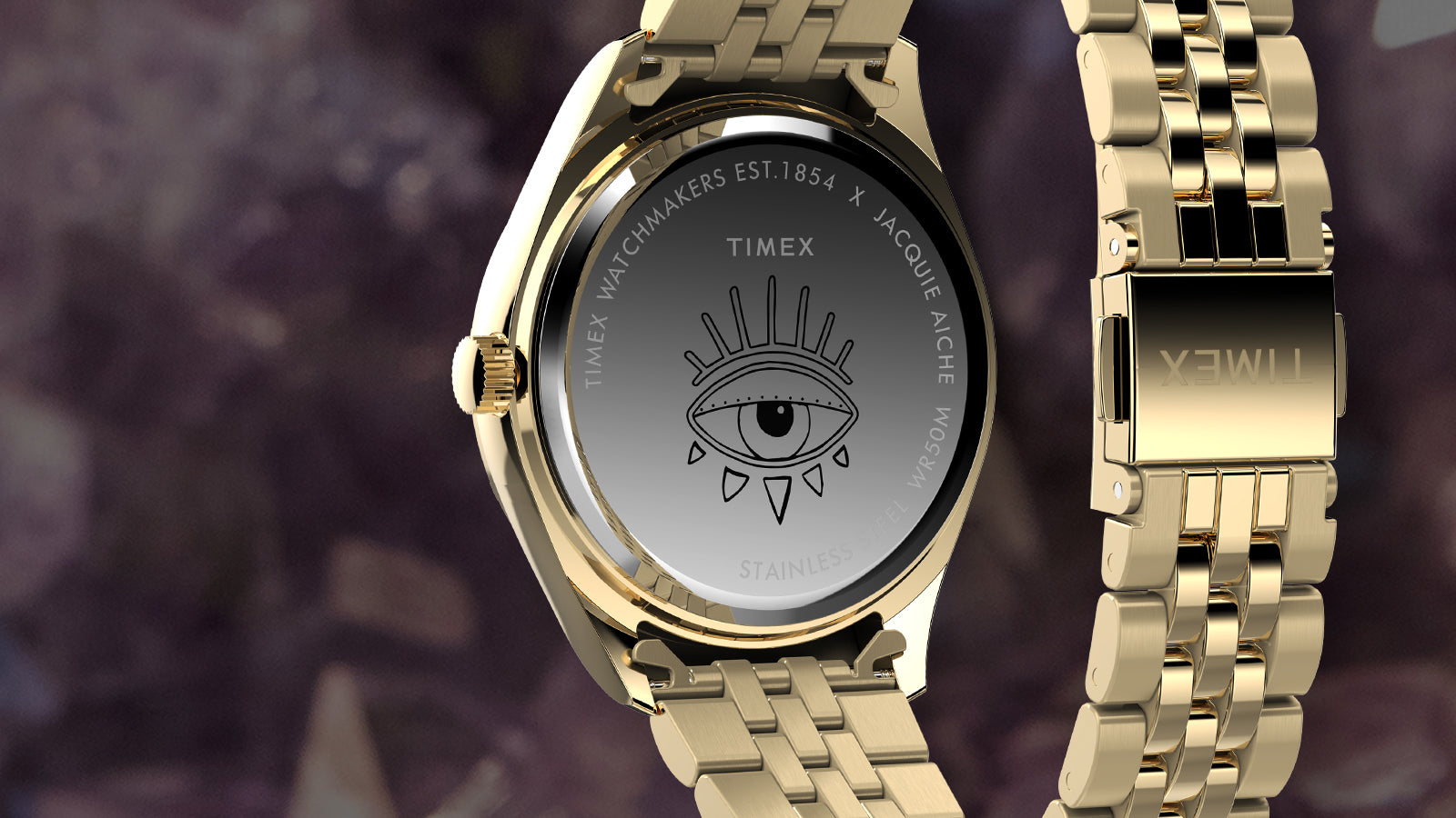 Rear view of the Timex x Jacquie Aiche “Cosmic Nights” watch showing the engraved cosmic eye symbol on the case back with co-branded text, paired with a gold-tone bracelet clasp engraved with the Timex logo.