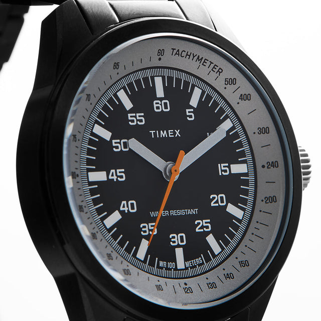 A close-up view of the Huckberry x Timex 1979 Black Max watch face, showing detailed white markers, the tachymeter scale, and the bright orange seconds hand against the black dial.