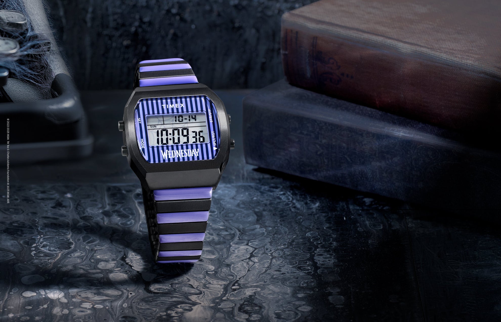 Timex x Wednesday T80 digital watch featuring a black and purple striped design on the face and bracelet. The watch is displayed on a dark, moody surface beside vintage books, evoking a gothic aesthetic inspired by Wednesday Addams.
