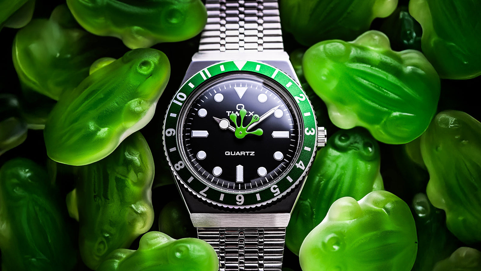 Timex x seconde/seconde/ Q Timex with a stainless-steel bracelet nestled among green frog-shaped candies. The frog foot hour hand adds a whimsical twist to the otherwise classic dive-style watch.