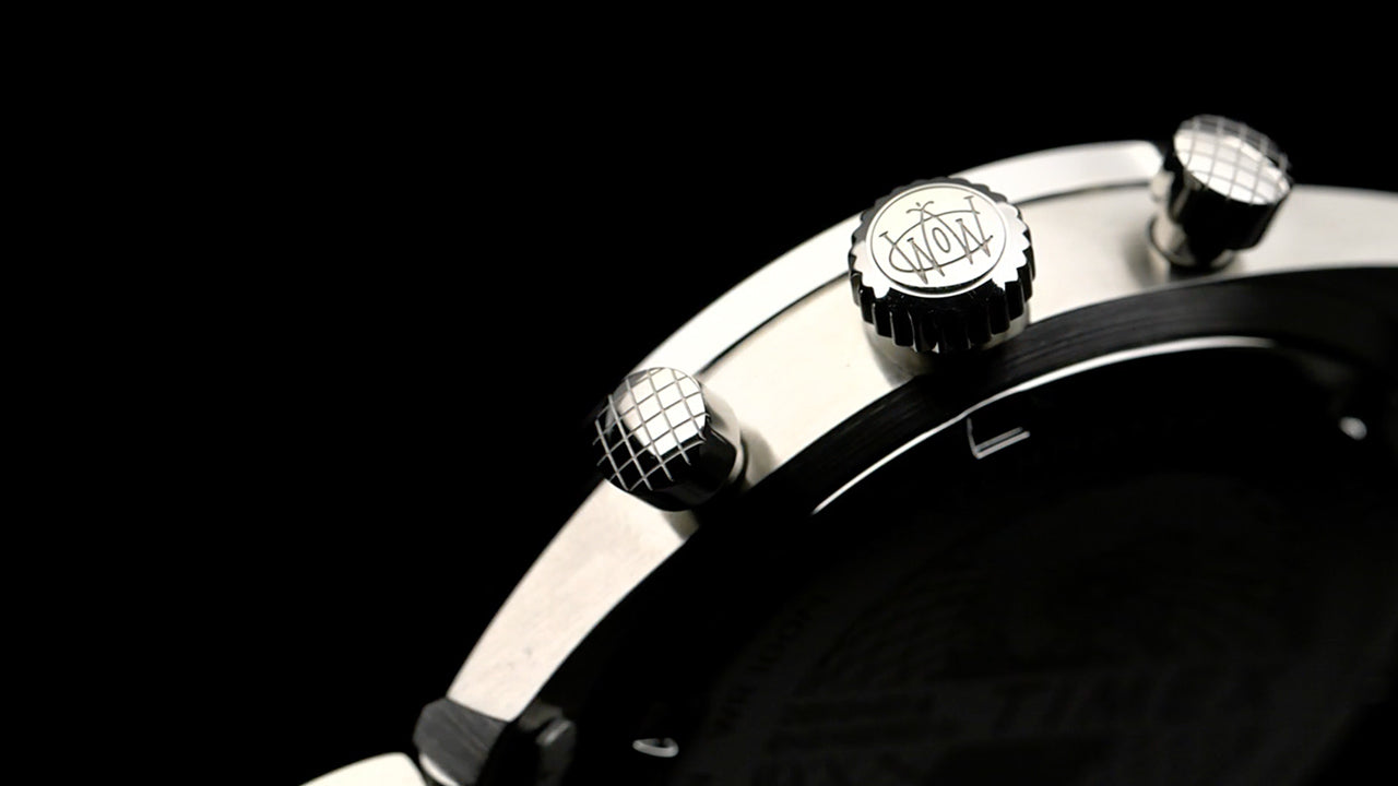 Detailed close-up of the Timex Waterbury Chronograph crown and pushers engraved with the Waterbury logo, showing brushed stainless steel finish.