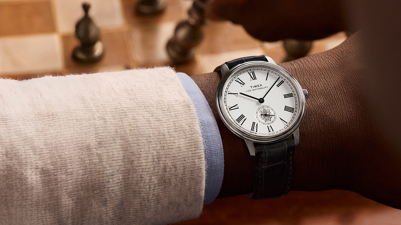 Timex Waterbury Metropolitan Sub-Second watch on wrist, displaying classic white dial and black leather strap during a chess game.